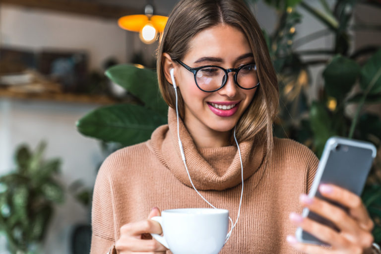 woman wearing glasses and a sweater smiling at her phone in a cafe